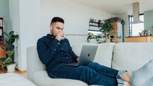 man in blue jacket and blue denim jeans sitting on gray sofa using macbook